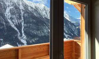 A view from a window of the majestic snow-covered mountains. The wooden balcony provides a cozy view of the impressive landscape.
