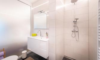 A modern bathroom with a shower and a white sink. The walls are brightly tiled, and there is a large mirror surface.
