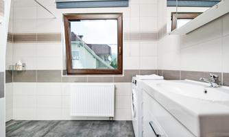 A modern bathroom with a window and a sink. On the right side, there is a washing machine and the walls are painted in light colors.