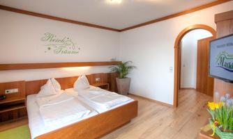 A cozy room with a double bed and minimalist wooden decor.  
On the wall, there is the inscription "Realm of Dreams" and a plant provides a pleasant atmosphere.