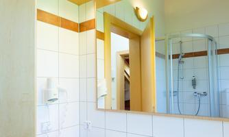 A modern bathroom with a large mirror and bright lighting. The sink is made of white porcelain and there is a shower cubicle in the background.