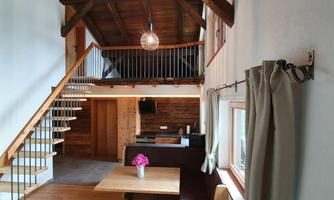 A bright, modern apartment with a wooden staircase and an open living area. A table with a flower and cozy seating invite you to linger.