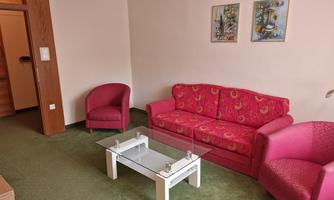 A cozy living room with a red sofa and two armchairs. A glass table is in the middle on green carpet.