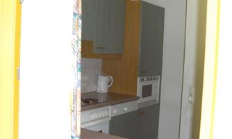 A small, modern kitchen with gray and wood-colored cabinets. On the countertop, there is a kettle and a microwave.