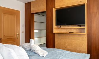 A modern bedroom with a large bed and a television on the wall. The wooden elements create a warm atmosphere.
