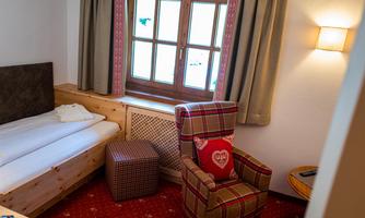 A cozy room with a single bed, an armchair, and a small table. Large windows provide plenty of daylight.