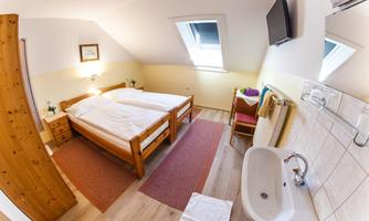 A cozy bedroom with two beds, wooden dressers, and a television. The room also features a sink and bright walls.