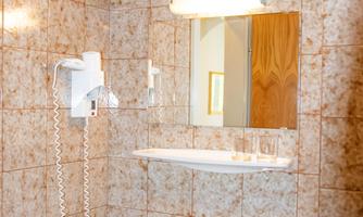A small bathroom with a sink unit and a mirror. The walls are decorated with beige-colored tiles.
