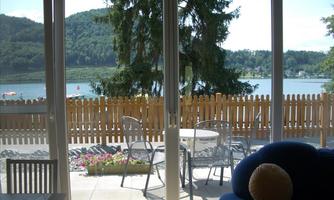 A cozy view of a lake from a modern room. Outside, there are chairs and a table with a view of nature.