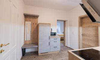 A modern kitchen with wooden furniture and a stove. The space is bright and friendly, with an open passage door to another room.