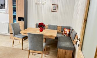 A cozy dining area with a wooden table and gray chairs. A flower vase and a decorative cushion are on the table.