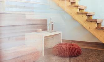 A modern room with a wooden staircase and a small table. On the floor, there are cozy poufs in orange.