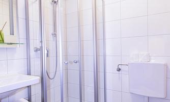 A modern bathroom with a shower and a toilet. There is a small table and bright, neutral wall tiles.