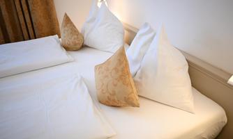 A cozy bedroom with a double bed and two large pillows. The pillows have decorative covers with a gold-colored pattern.