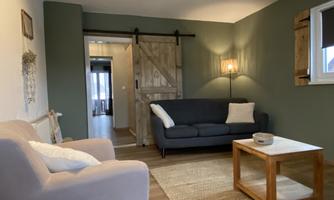 A cozy living room with a gray sofa and a wooden coffee table. The walls are painted green and there is a lamp that provides warm light.