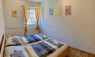A bright bedroom with two single beds and colorful wall paintings. The windows are decorated with orange curtains.