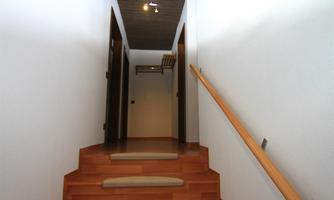 A bright hallway with a wooden staircase and doors on both sides. The walls are white and the floor is made of wood.