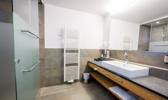 A modern bathroom with a wooden sink and a large mirror surface. The shower is separated by a glass wall.