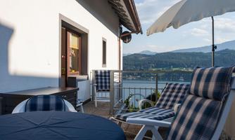 A cozy terrace with deck chairs and a table. In the background is a beautiful view of the lake and the surrounding mountains.