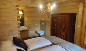 A cozy bedroom in a wooden house. It features a double bed, a wardrobe, and modern lighting.