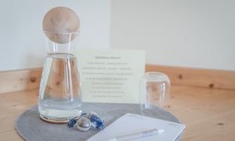 A glass of water with a wooden lid is on a table. Next to it are a notepad, a pen, and some small items.