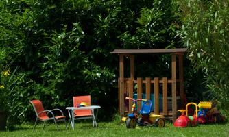 An inviting playground in the garden with a wooden hut and colorful toys. Two chairs and a table invite you to linger.
