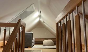 A bright attic with an open space and a cozy seating area. A wooden staircase leads to the upper area.