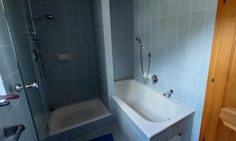 A modern bathroom with a shower and a bathtub. The walls are tiled in a light blue shade.