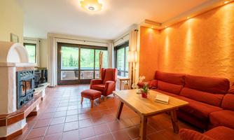 A cozy living room with red sofas and a wood stove. Large windows provide a view of the green surroundings.
