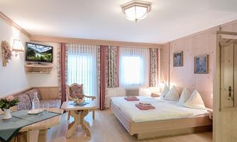 A cozy bedroom with a double bed and a seating area. Large windows provide plenty of daylight and a pleasant atmosphere.