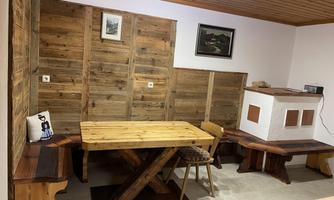 A cozy dining area with a large wooden table and wooden bench. The walls are lined with wood paneling and there is a small fireplace heater.