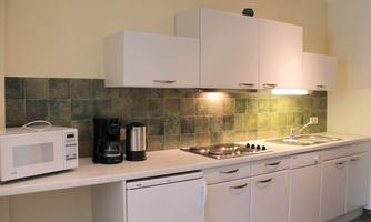 A modern kitchen with white furniture and a green tiled backsplash. There is a microwave, a coffee machine, and a stove.
