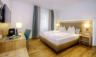A modern hotel room with a double bed and two pillows. There is a desk, a television, and large windows that let in plenty of daylight.