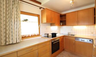 A modern kitchen with wooden cabinets and a window that lets in a lot of light. The countertop is clean and tidy, with a stove and a sink.