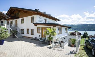 A modern house with a beautiful view of the lake. In the foreground, there is a cozy terrace and well-maintained plants.