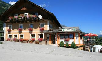A traditional Alpine building with flower boxes and wooden cladding. It houses the restaurant "Stadlwirt" and offers a view of the surrounding landscape.