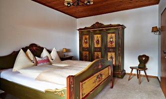 A cozy bedroom with an artistically decorated bed and a colorful wardrobe. The warm wooden ceiling and soft lighting create an inviting atmosphere.