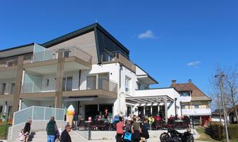 A modern building with a terrace where many people are standing. The sky is clear and blue, indicating nice weather.