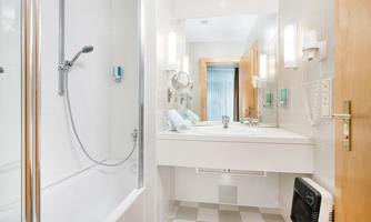 A modern bathroom with a bathtub and shower. There is a washing area with a mirror and ample lighting.