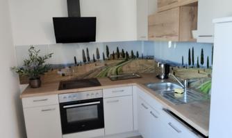 A modern kitchen with wooden shelves and a stove. In the background, there is a mural-like landscape featuring cypress trees.