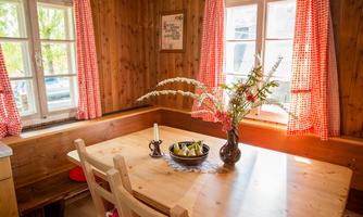 A cozy dining area with a wooden table and chairs. On the table is a vase with flowers and a bowl of fruits.