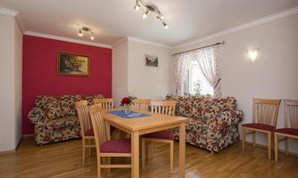 A bright living room with two sofas and a dining table. The walls are partially painted red and large windows let in a lot of light.