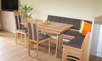 A cozy dining area with a wooden table and chairs. The seating area is decorated with a cushion, and a bowl of fruit is on the table.