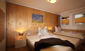 A cozy bedroom with wooden walls and a double bed. There is a small seating area, nightstands, and a bright window.