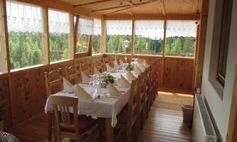 A sunny dining area with a large table and wooden chairs. The windows offer a beautiful view of the surrounding nature.