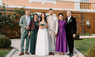 A wedding celebration with six people in formal attire. They are standing in a beautiful garden in front of an elegant building.