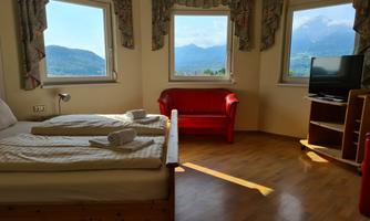 A bright room with two beds, a red sofa, and a television. Large windows provide a beautiful view of the mountains.