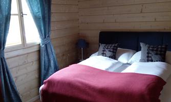 A cozy bedroom with wooden walls and a large bed. Curtains in blue and a red blanket give the room an inviting atmosphere.