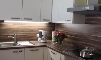 A modern kitchen with white cabinets and a wooden countertop. On the counter are a coffee machine and a vase of flowers.