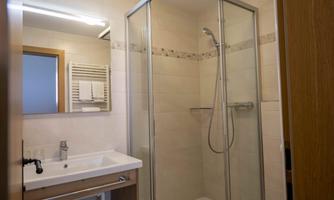 A modern bathroom with a shower and sink. The walls are brightly tiled, and a large mirror provides additional light.
